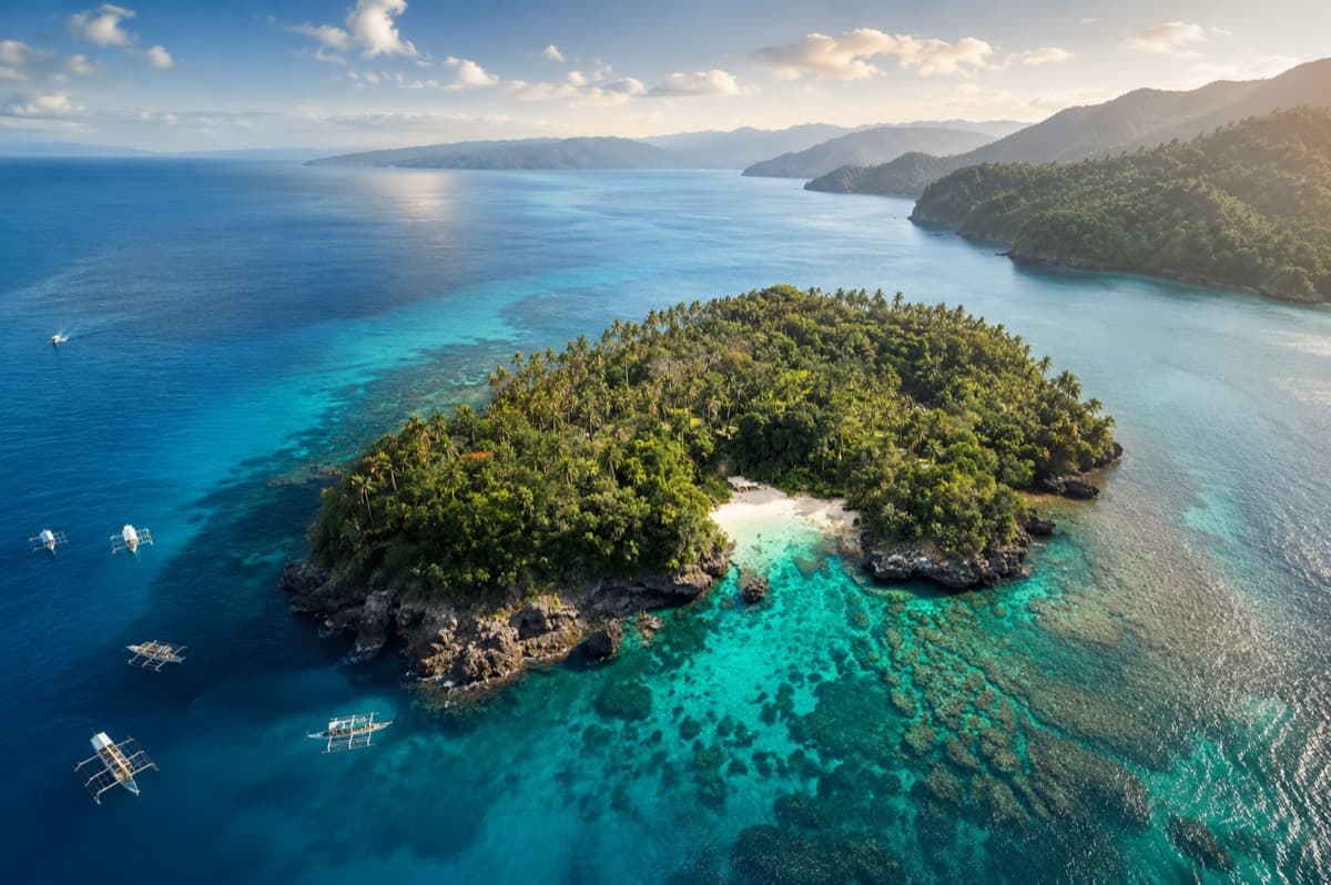 Aerial view of a palm-covered island off Puerto Galera, ringed by turquoise water and outrigger banca boats